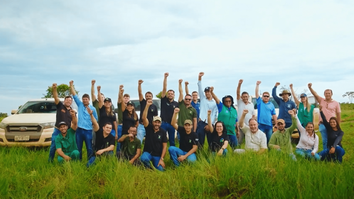 Equipe do Grupo RZK e parceiros em uma área verde, comemorando com os braços erguidos, destacando união e ações de sustentabilidade ambiental.