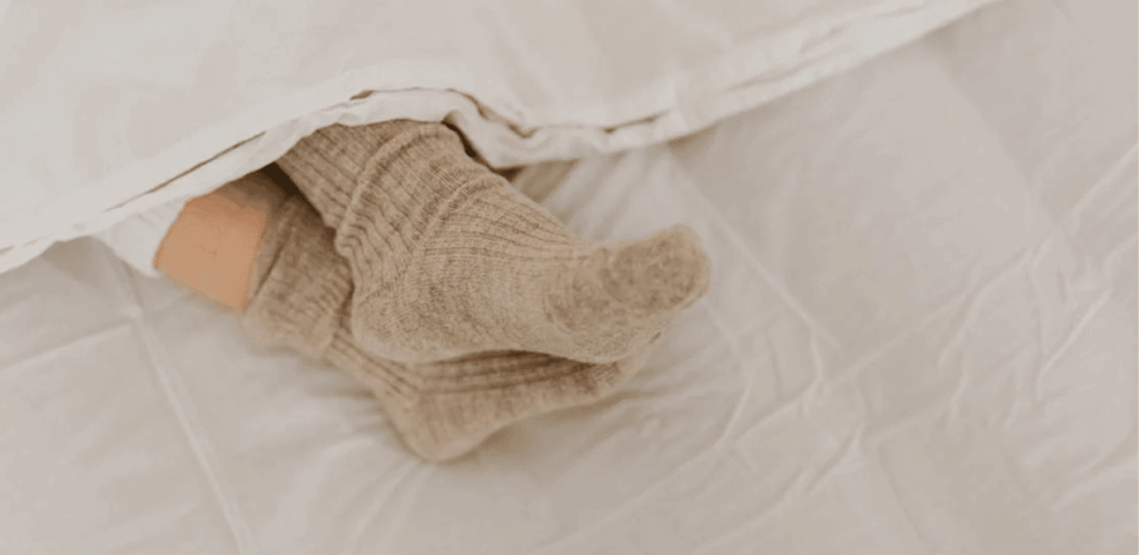 Pessoa dormindo com meia de lã sob cobertor, representando o uso de meias para melhorar a qualidade do sono.