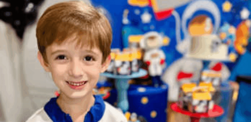 Menino superdotado de 5 anos sorri em festa temática, com decoração infantil ao fundo representando seu interesse por astronomia.