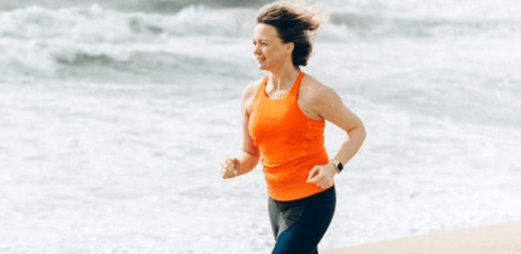 Mulher correndo na praia como parte da construção de hábitos saudáveis.