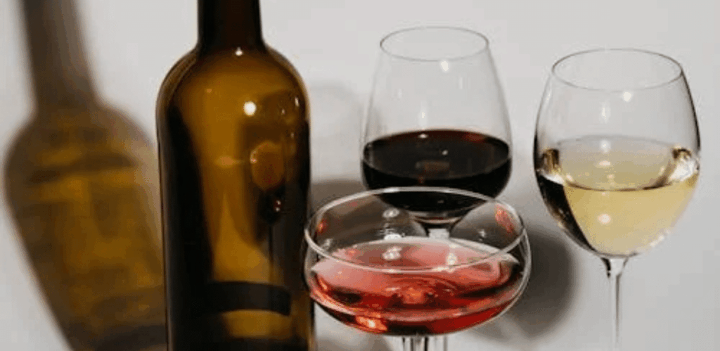 Taças com vinho tinto, branco e rosé representam estudo sobre os efeitos do vinho na saúde bucal por suas propriedades antibacterianas.