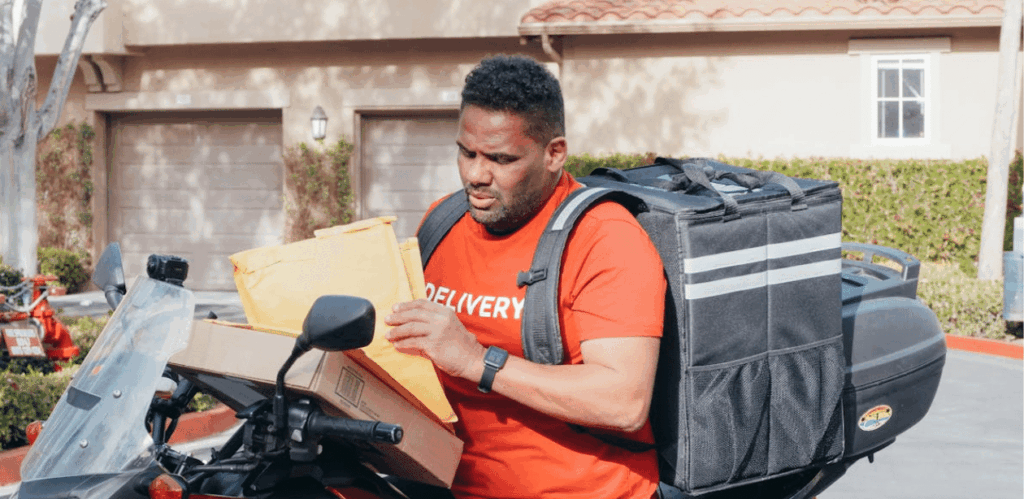 Motoboy com mochila de entrega manuseando pacotes sobre a moto, representando uma nova lei de segurança reforçada com rastreamento em SP.