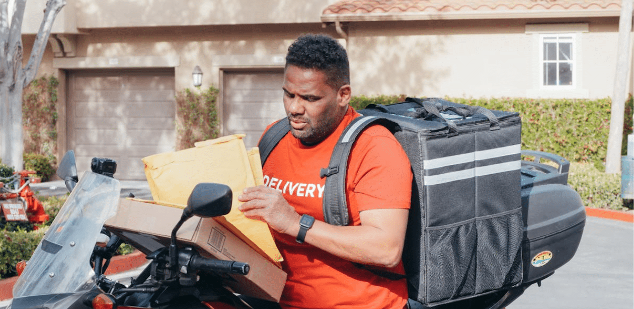 Motoboy com mochila de entrega manuseando pacotes sobre a moto, representando uma nova lei de segurança reforçada com rastreamento em SP.