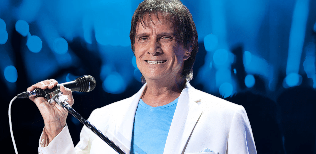 Roberto Carlos sorrindo ao microfone durante especial de fim de ano na TV, em negociação com a Globo após fim de contrato exclusivo.