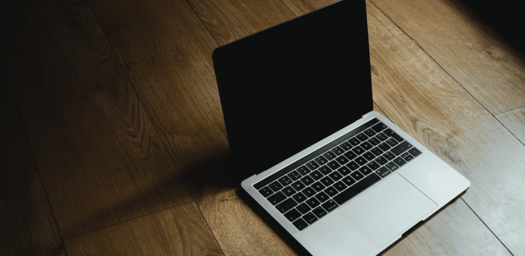 Notebook preto aberto sobre piso de madeira com tela desligada