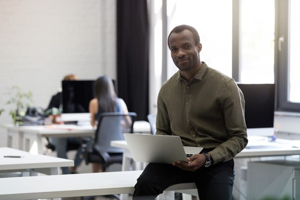 Homem negro em ambiente corporativo, sentado com notebook no colo, representando diversidade em cargos de liderança.