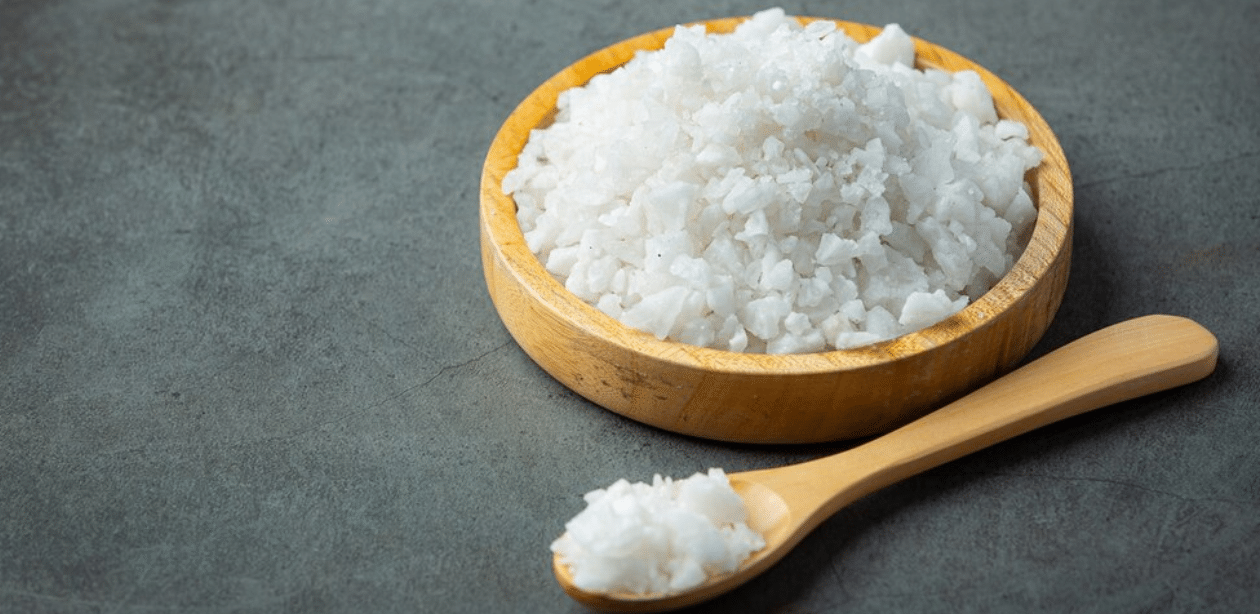 Tigela de madeira com sal grosso e colher ao lado, representando a importância de reduzir consumo de sal na alimentação