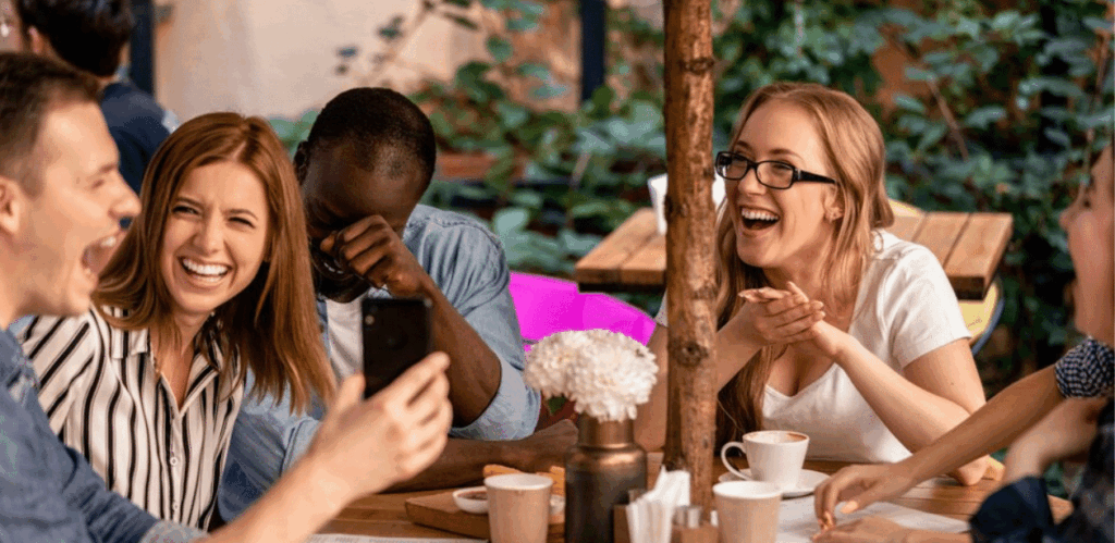 Pessoas sorrindo e conversando em mesa de cafeteria ao ar livre durante o dia, ilustrando a tendência de festas em cafeterias.