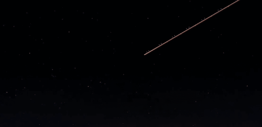 Céu noturno estrelado com rastro luminoso de meteoro cruzando a atmosfera durante uma chuva de meteoros