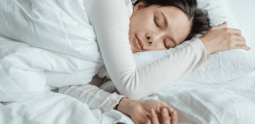 Pessoa dormindo tranquilamente na cama, representando os benefícios dos exercícios e sono de qualidade para o desempenho físico.