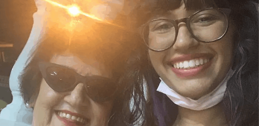 Idosa e jovem sorrindo juntas em casa intergeracional, representando convivência entre gerações e combate à solidão