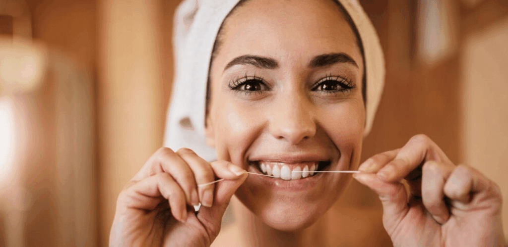 Mulher usando fio dental como parte da higiene bucal que ajuda a reduzir o risco de derrame e melhorar a saúde do coração.