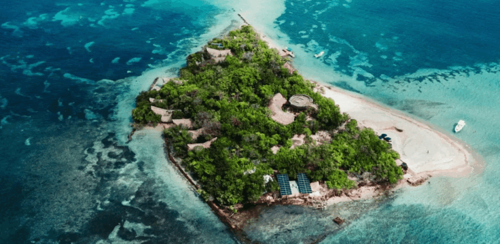 Imagem aérea da Ilha Corona na Colômbia, cercada por águas cristalinas do Caribe, com bangalôs sustentáveis em meio à vegetação.