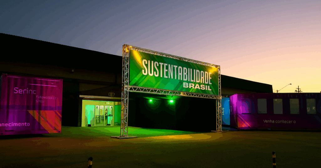 Entrada iluminada do Evento Sustentabilidade Brasil com estrutura metálica e painel verde ao entardecer