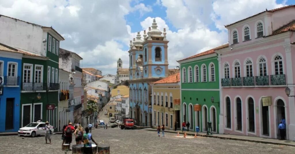 Pessoas caminhando por rua de paralelepípedos entre casarios históricos coloridos em cidade brasileira com arquitetura colonial