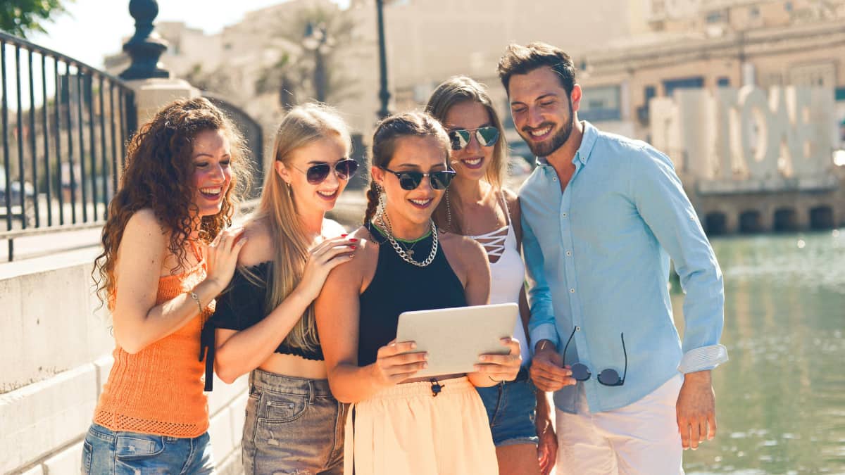 Grupo de jovens curtindo uma viagem em grupo com amigos ao ar livre, usando tablet para organizar atividades