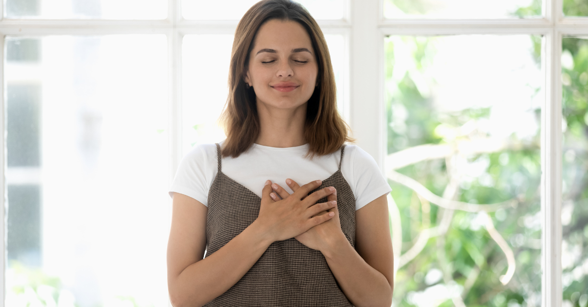 Mulher com a mão no peito e olhos fechados, expressando gratidão e serenidade.