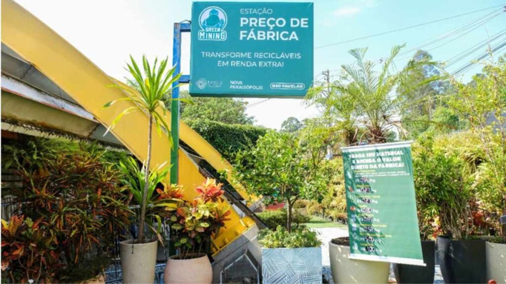 fachada da Estação Preço de Fábrica da Green Mining em Paraisópolis, com vegetação, placa de preços e sinalização do projeto de reciclagem na periferia