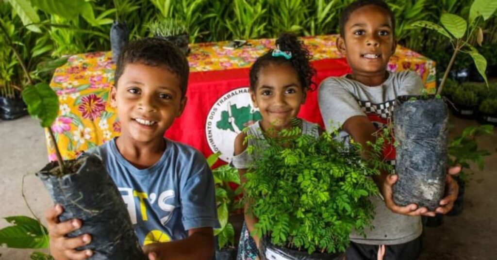 Crianças seguram mudas durante ação de reflorestamento popular no Brasil do MST 
