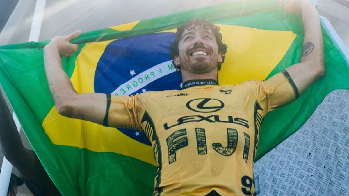 título mundial de Yago Dora- : Yago Dora comemora título mundial de surfe 2025 em Fiji, erguendo a bandeira do Brasil após vencer a final da WSL.