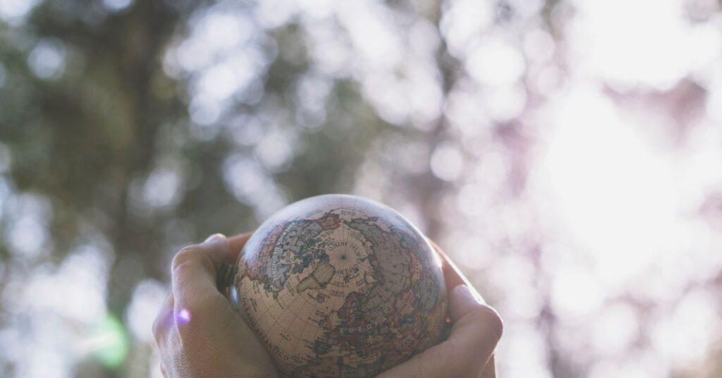 Mãos segurando um pequeno globo terrestre com fundo natural, representando a adaptação da saúde ao clima.
