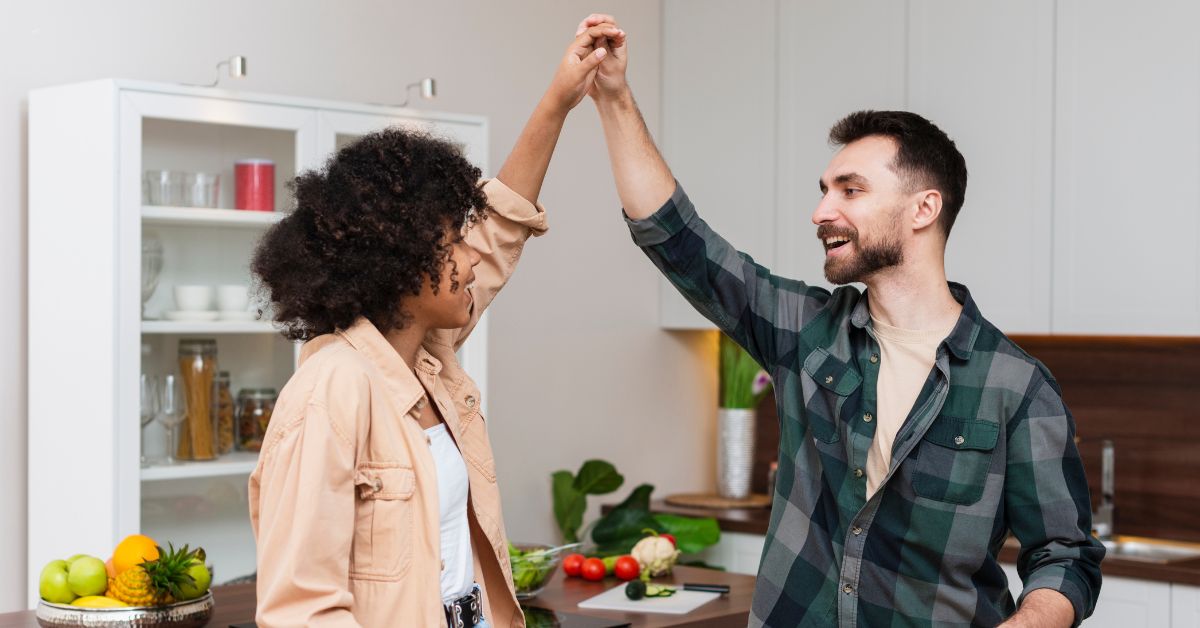 leituras sobre relacionamentos - Casal sorridente dançando juntos na cozinha, representando alegria e harmonia nas relações.