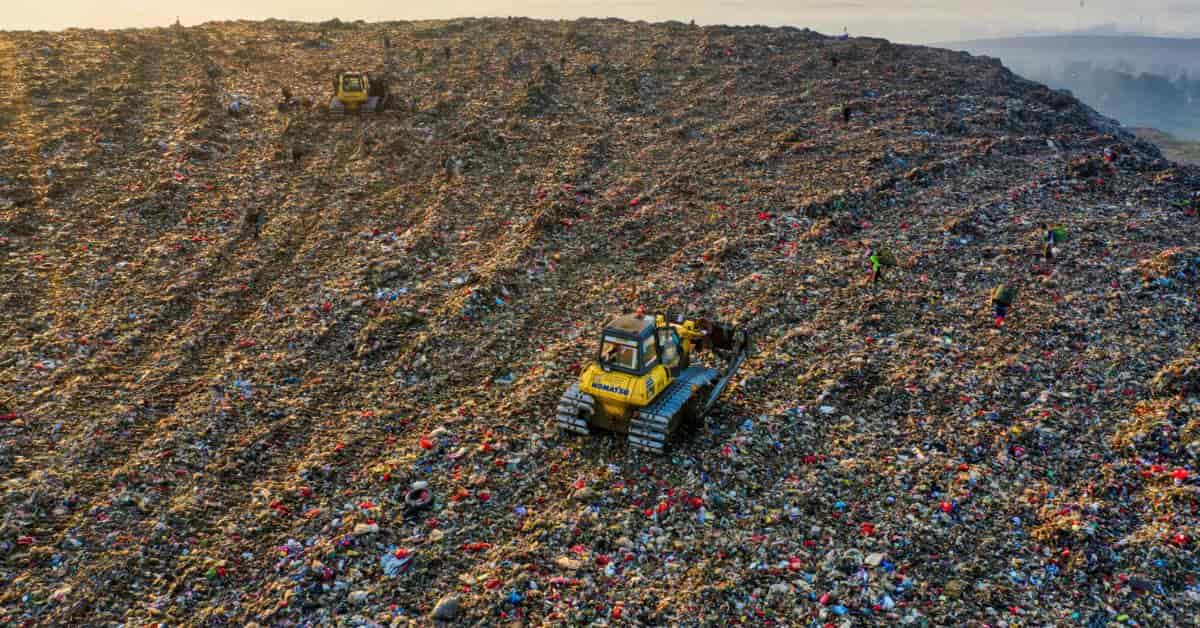 Aterro sanitário com toneladas de resíduos têxteis e máquinas em operação, simbolizando a urgência da reciclagem na moda na Europa.