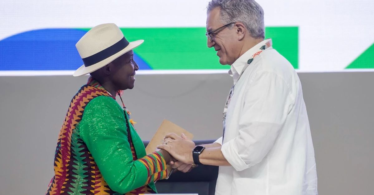 Plano de Ação em Saúde de Belém - Pessoa com chapéu claro e roupa tradicional colorida cumprimenta um representante da COP30 vestido com camisa branca, durante evento oficial em Belém.