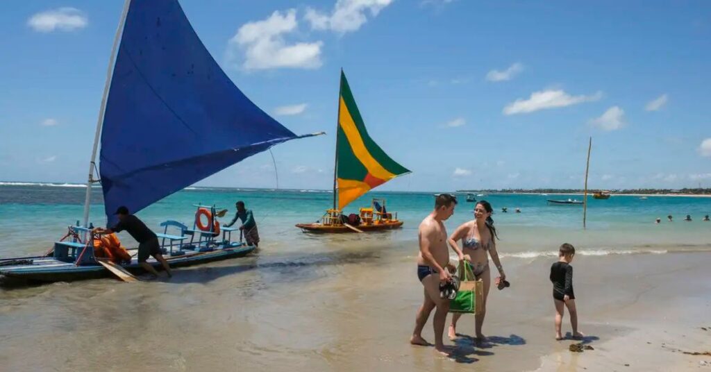Turistas aproveitam praia brasileira com jangadas coloridas, cenário que simboliza o Brasil turismo internacional em alta.