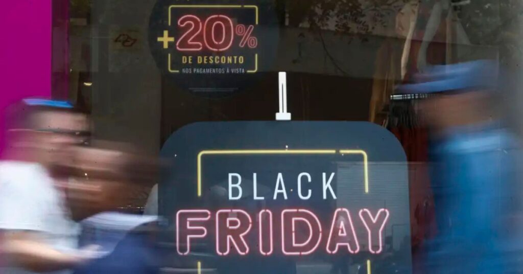 Vitrine com anúncio de descontos da Black Friday Brasil e pessoas passando em frente à loja.