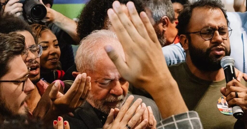 Cena registrada em Apocalipse nos Trópicos mostra momento de oração em grupo durante evento político no Brasil.