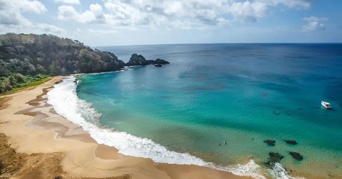 Vista aérea de Fernando de Noronha com mar azul e praia preservada, reforçando o avanço do arquipélago rumo à energia limpa.