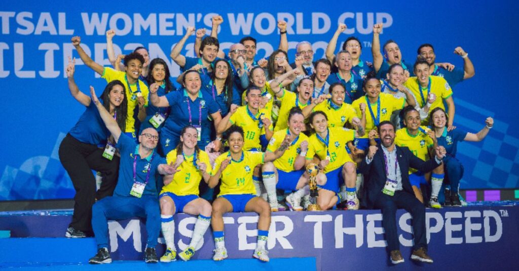 Seleção Brasileira Feminina de Futsal comemora título inédito da Copa do Mundo com equipe reunida no pódio.