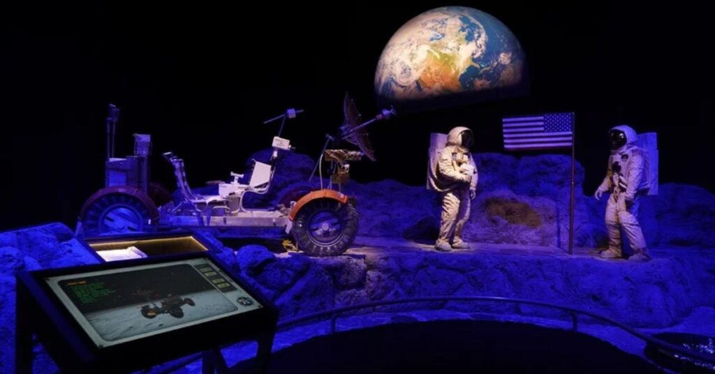 Exposição interativa sobre ciência e tecnologia com astronautas, módulo lunar e a Terra ao fundo em museu no Brasil
