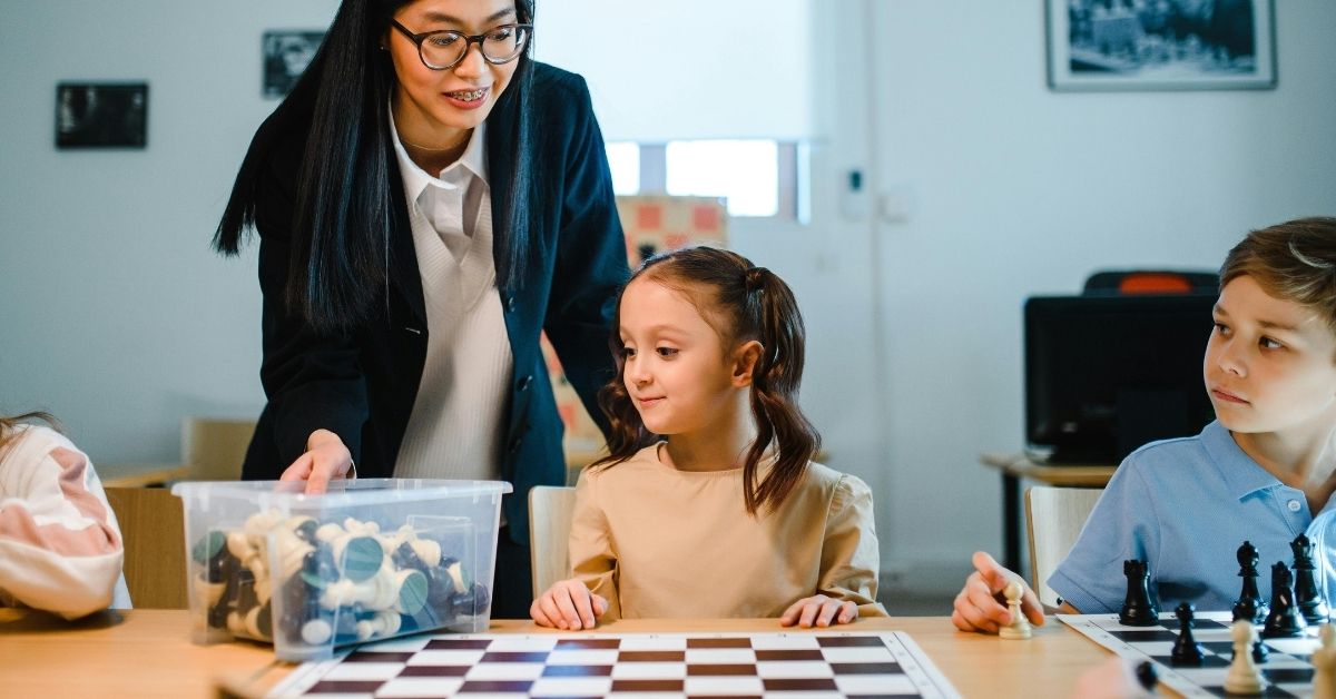 professora orienta crianças durante atividade com jogos de tabuleiro em sala de aula