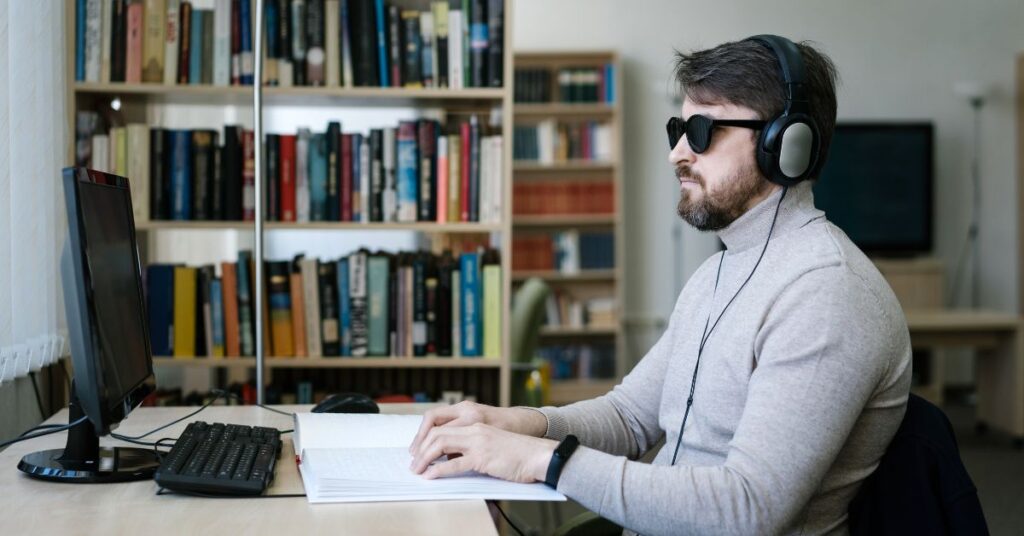 Homem com deficiência visual utiliza computador e livro em braille na educação para cegos Brasil